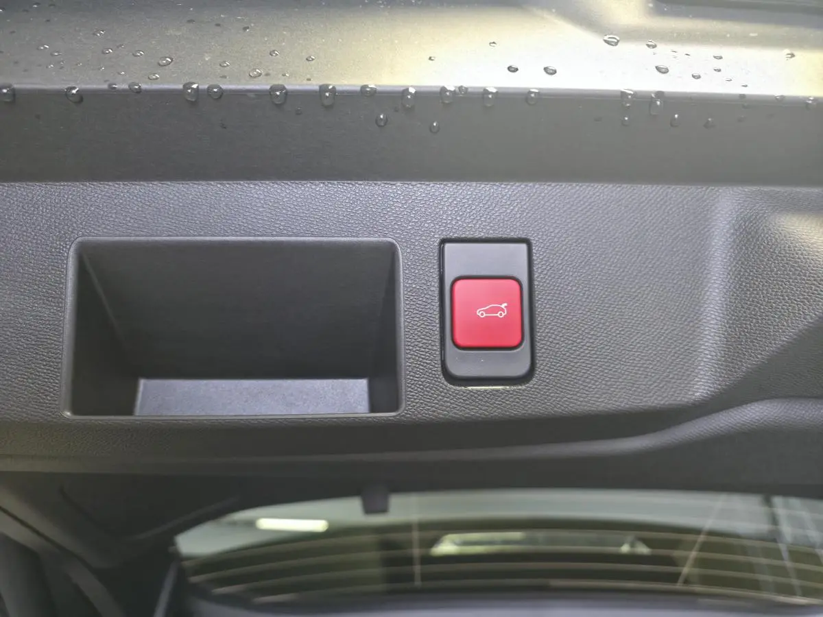Détail du bouton rouge d'ouverture électrique du hayon sur le bord intérieur du coffre d'une Citroën C5 Aircross vert.
