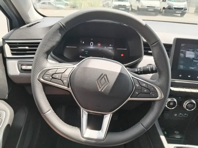 Vue rapprochée du volant noir perforé de la Renault Clio V TCE 90 Evolution 2026 avec tableau de bord numérique et commandes intégrées.