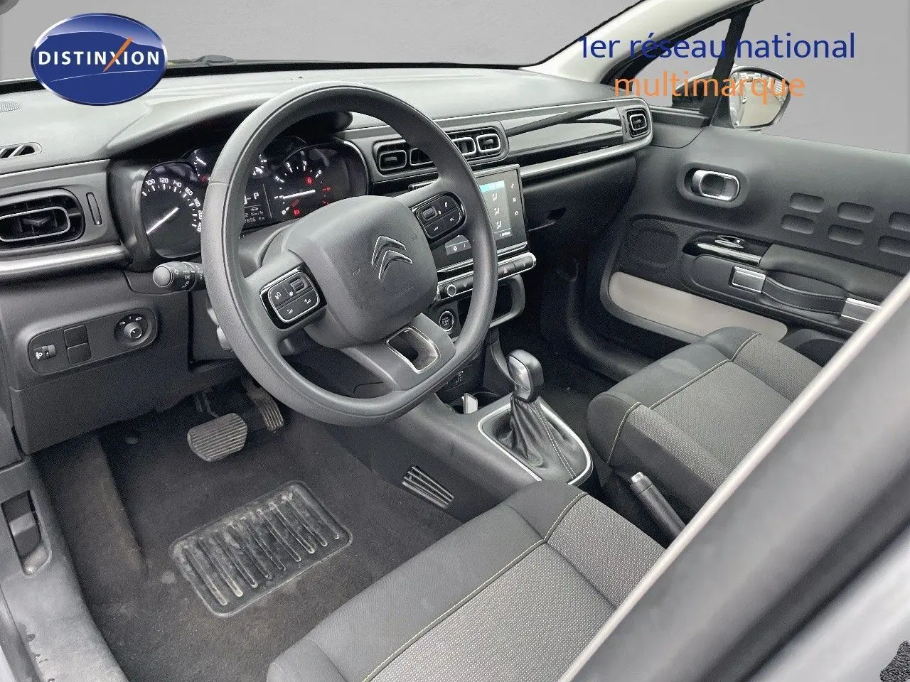 Intérieur de la Citroën C3 2023 côté conducteur, tableau de bord moderne avec volant multifonction et sellerie tissu gris.