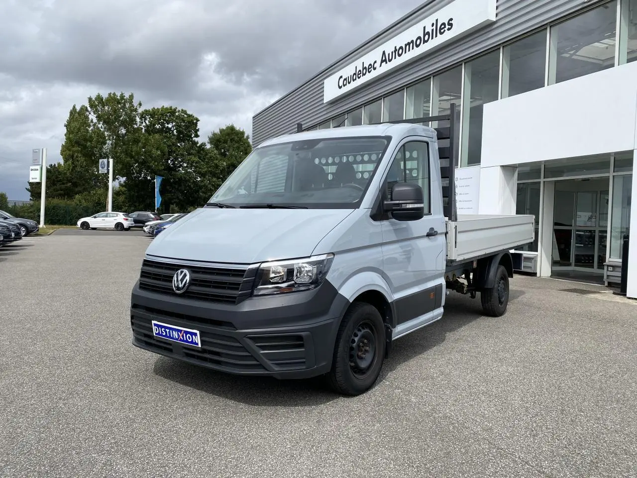 Volkswagen Crafter Fourgon gris argent vu en 3/4 avant droit avec plateau ridelles et calandre noire.