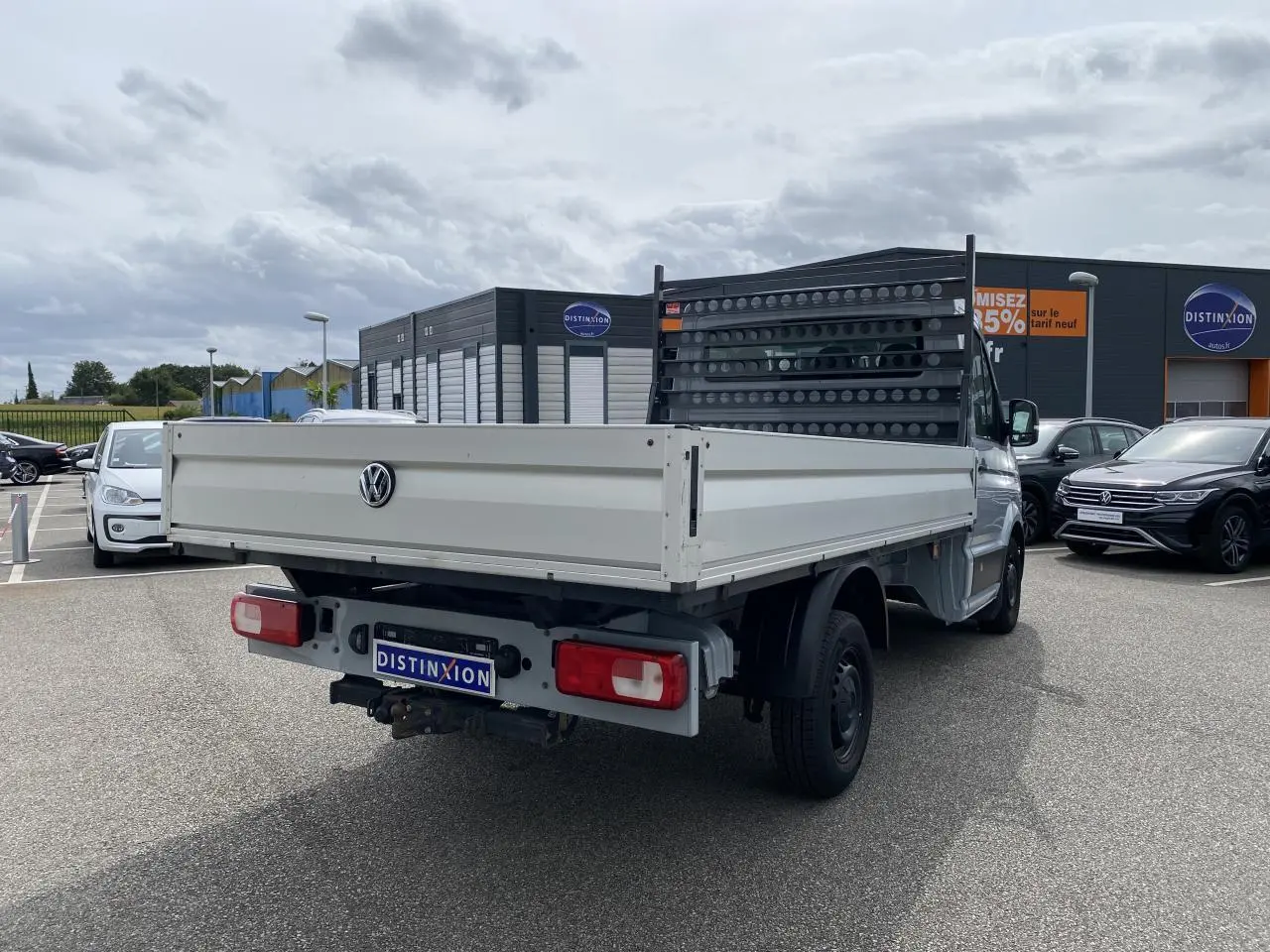 Vue 3/4 arrière droite d'un Volkswagen Crafter fourgon gris argent avec plateau et attelage rigide visible.