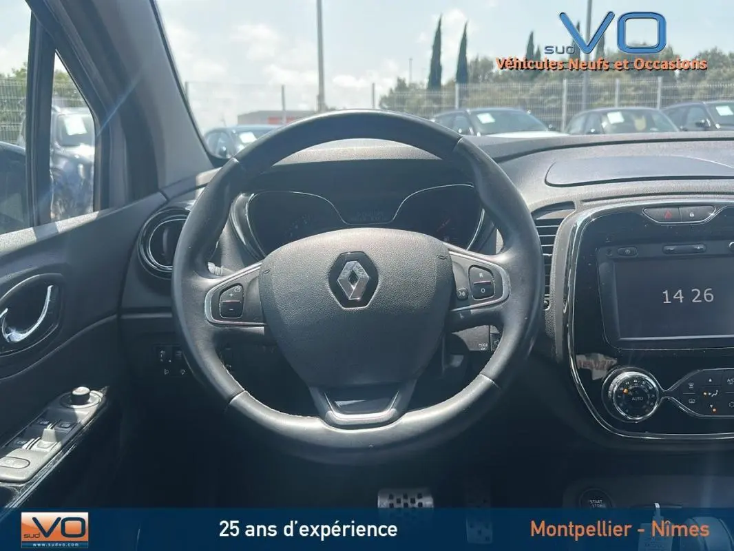 Vue centrée sur le volant cuir et tableau de bord du Renault Captur gris clair, avec écran tactile et commandes au volant visibles.