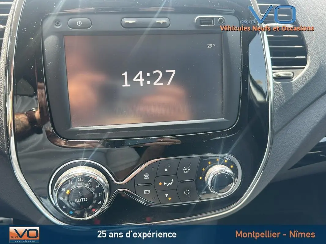 Gros plan sur la console centrale noire brillante du Renault Captur gris clair, affichant l'heure et les commandes de climatisation.