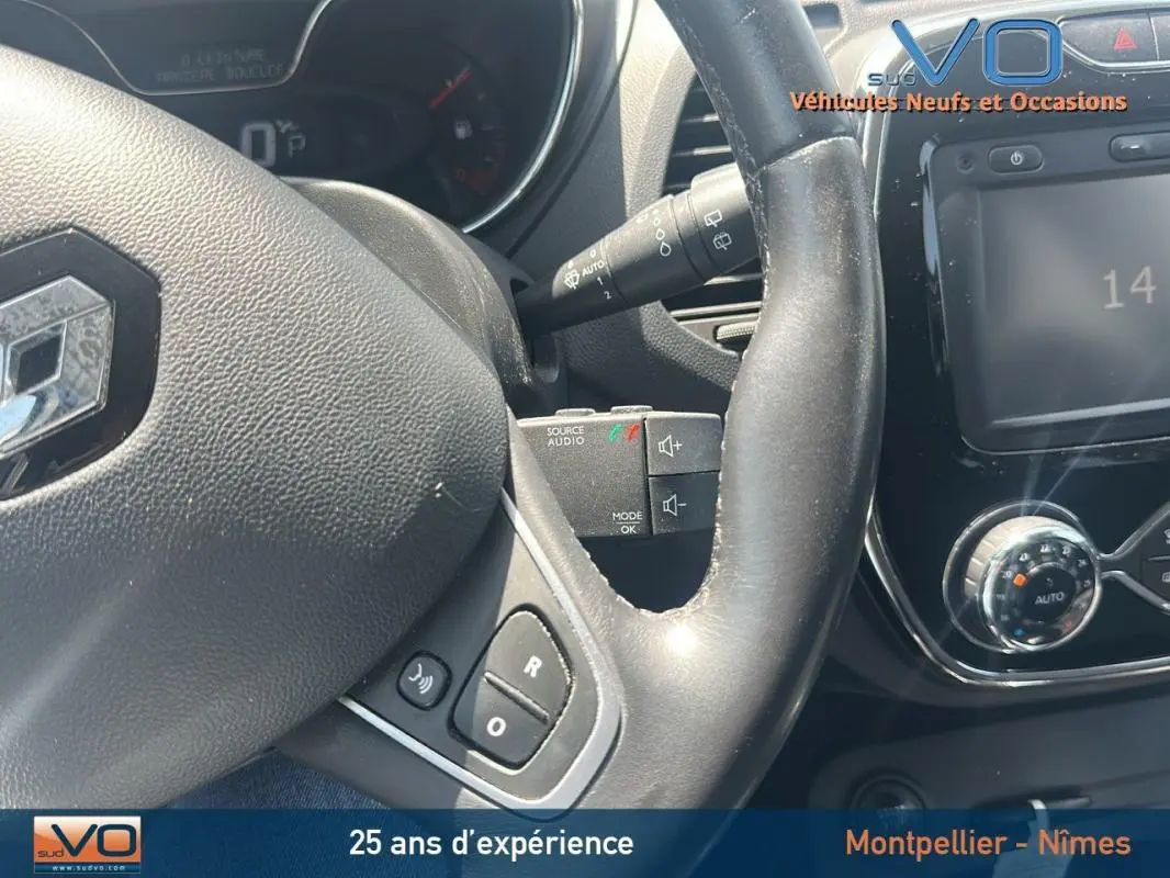 Gros plan sur le volant cuir et la console centrale du Renault Captur gris clair, mettant en valeur les commandes audio et climatisation manuelle.