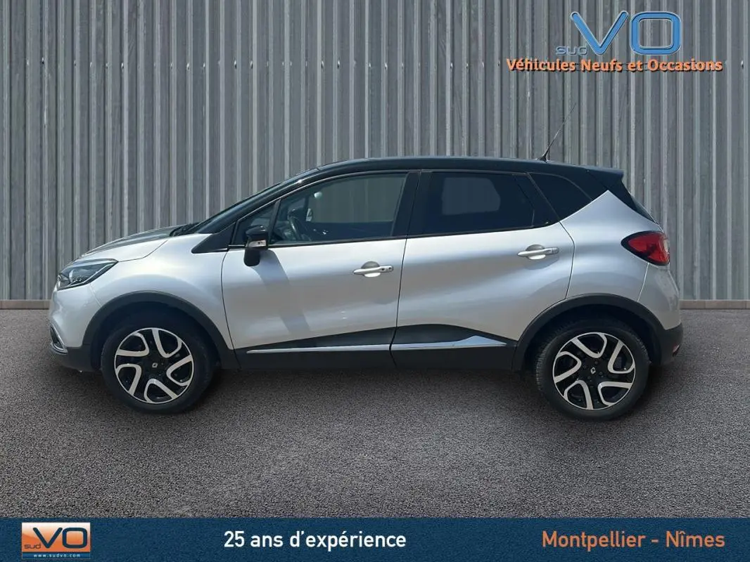 Profil côté gauche d'un Renault Captur gris clair 2016 avec jantes alliage et toit noir sur fond industriel.