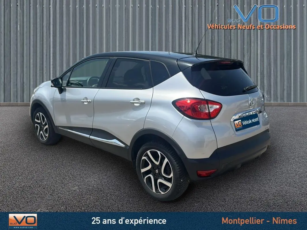 Vue 3/4 arrière droite d'un Renault Captur gris clair avec toit noir et jantes alliage 16 pouces sur sol goudronné.