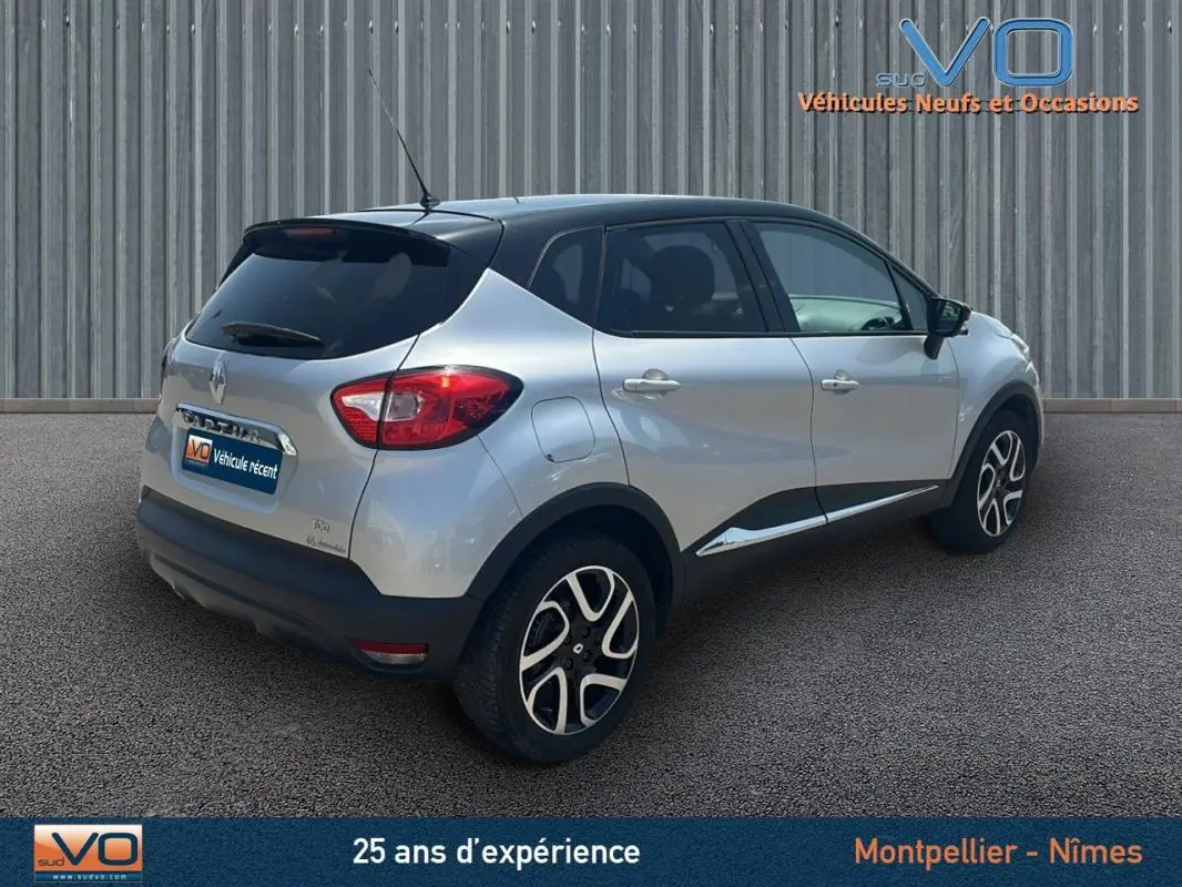 Vue 3/4 arrière droite d'un Renault Captur gris clair avec jantes alliage et toit noir sur fond industriel.