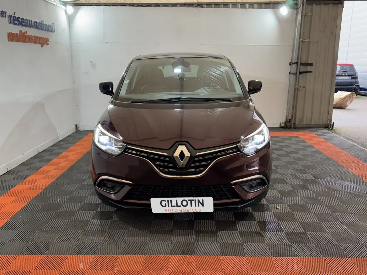 Renault Scénic Intens rouge vue de face avec phares allumés dans un garage au sol damier noir et orange