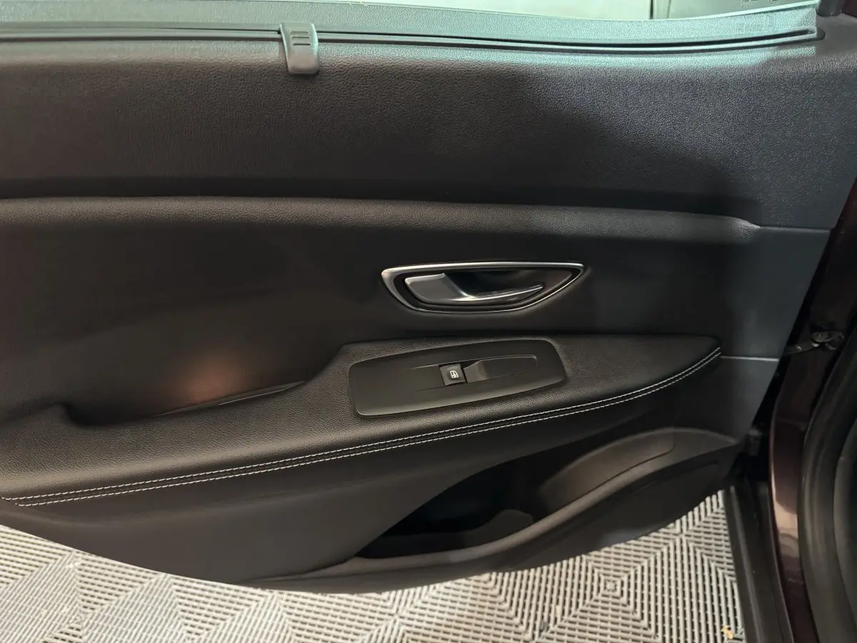 Gros plan sur la porte intérieure côté droit du Renault Scénic Intens rouge, avec poignée argentée et commande de vitre noire.