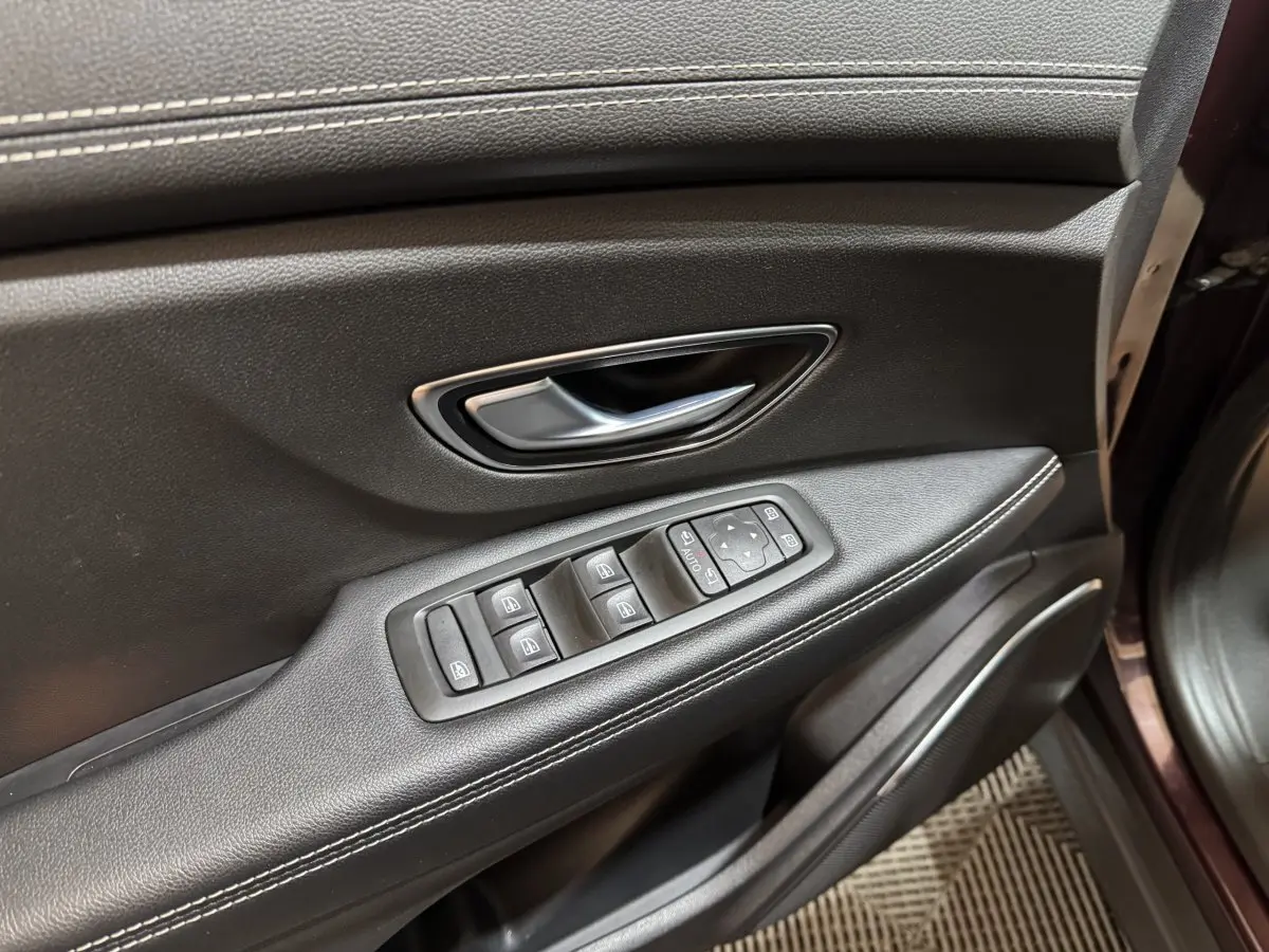 Gros plan sur la porte avant gauche du Renault Scénic Intens rouge, avec commandes des vitres et poignée argentée.