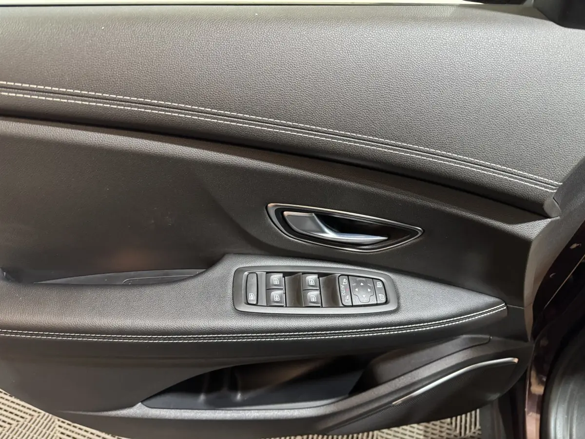 Gros plan sur la porte intérieure côté conducteur du Renault Scenic Intens rouge, avec commandes électriques et surpiqûres blanches.