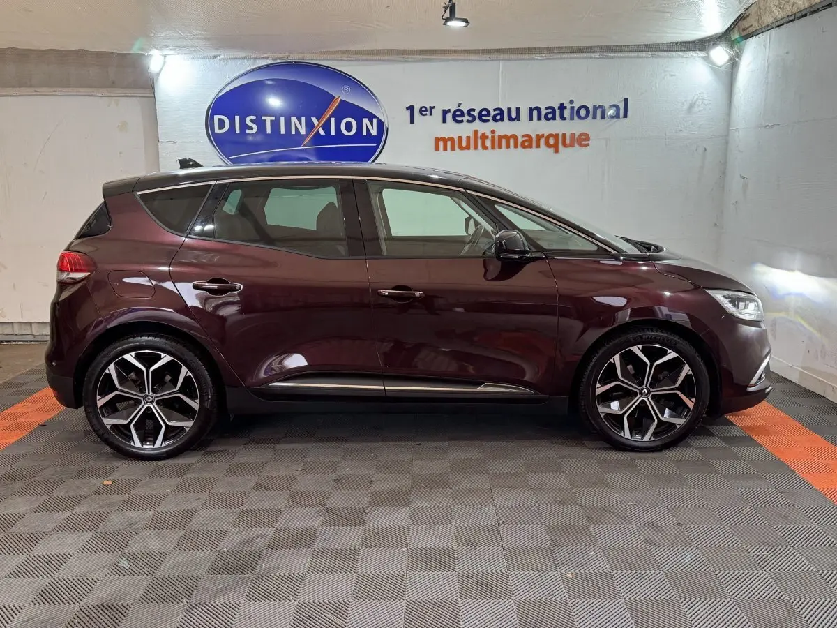 Profil droit d'un Renault Scénic Intens rouge foncé 2021 avec jantes alliage et vitres teintées en intérieur showroom.