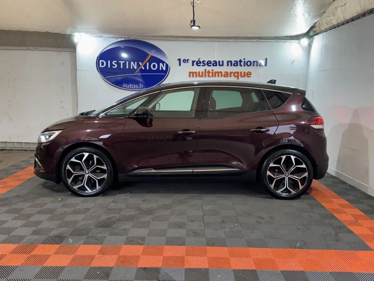 Profil droit d'un Renault Scénic Intens rouge foncé 2021 avec jantes alliage et vitres teintées en intérieur showroom.