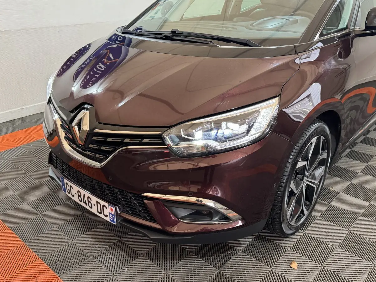Vue 3/4 avant droit d'un Renault Scénic Intens rouge avec phares LED allumés et jantes alliage noires.