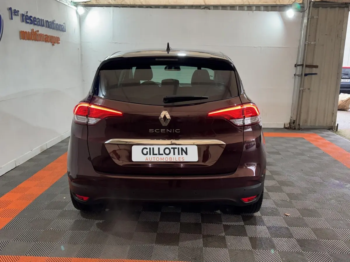 Vue arrière d'un Renault Scénic rouge foncé avec feux LED allumés, stationné dans un garage intérieur.