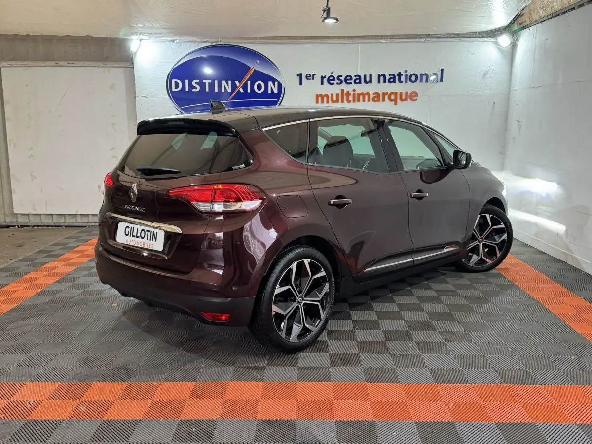 Renault Scénic rouge foncé vue 3/4 arrière droit en intérieur avec jantes alliage et vitres teintées.