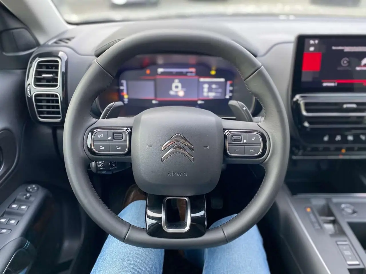 Vue intérieure centrée sur le volant noir du Citroën C5 Aircross 2025 avec tableau de bord numérique et écran tactile.