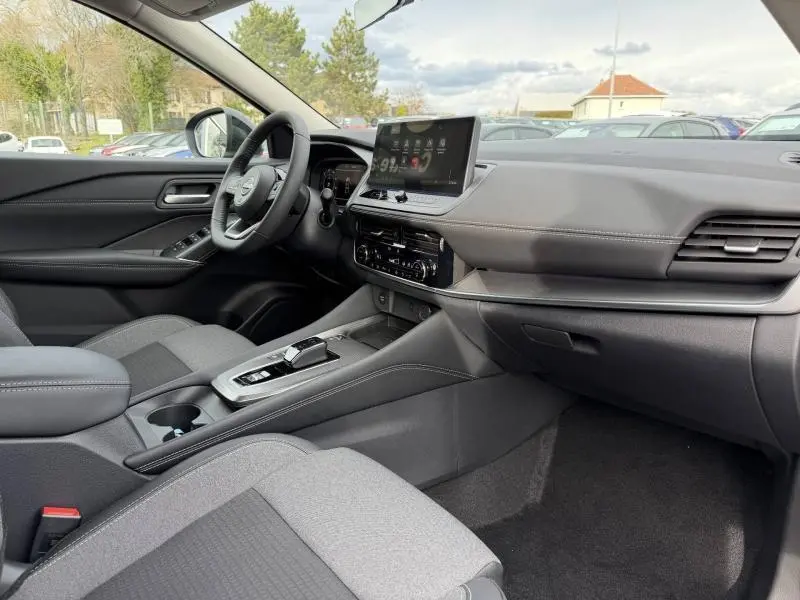 Intérieur du Nissan Qashqai Hybrid e-POWER 2025 vu côté passager, avec tableau de bord noir et sièges tissu mixte gris.