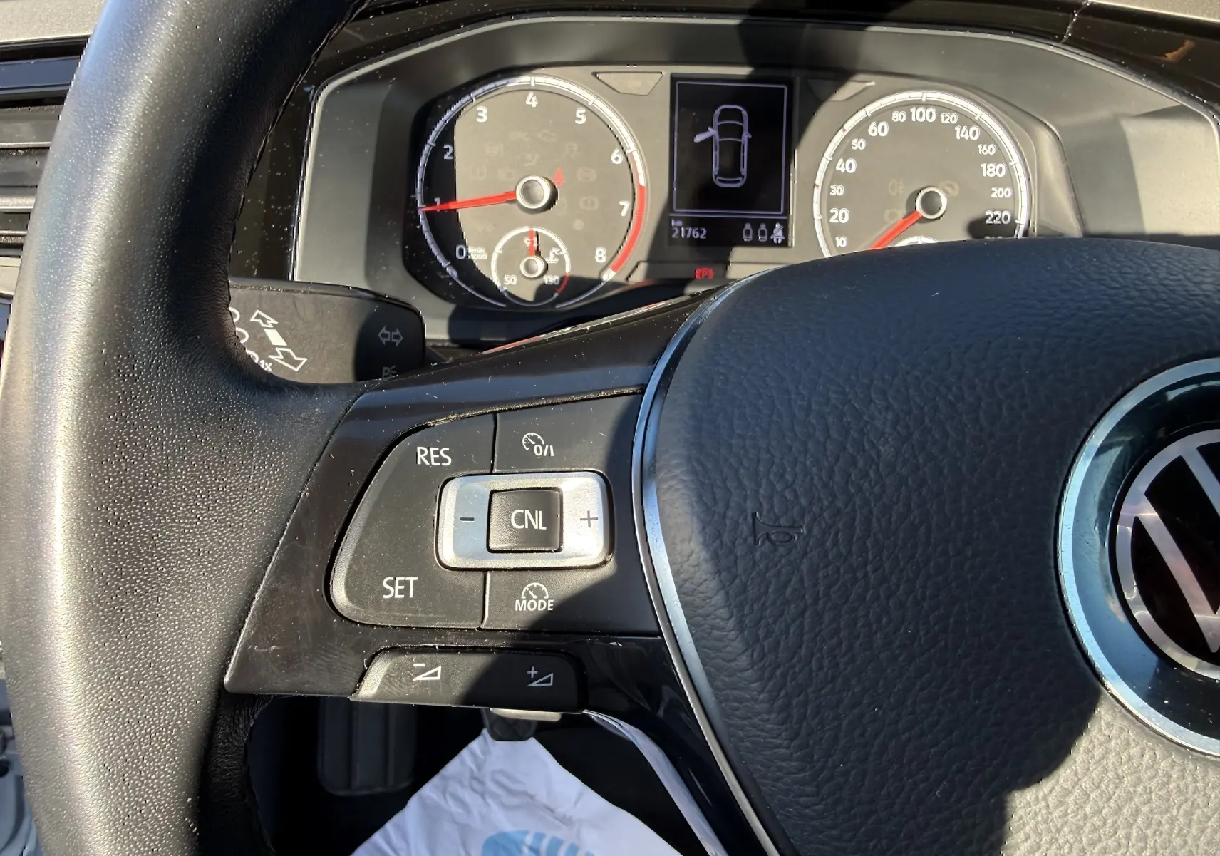 Gros plan sur le volant noir et le tableau de bord d'une Volkswagen Polo gris métal, avec commandes au volant visibles.