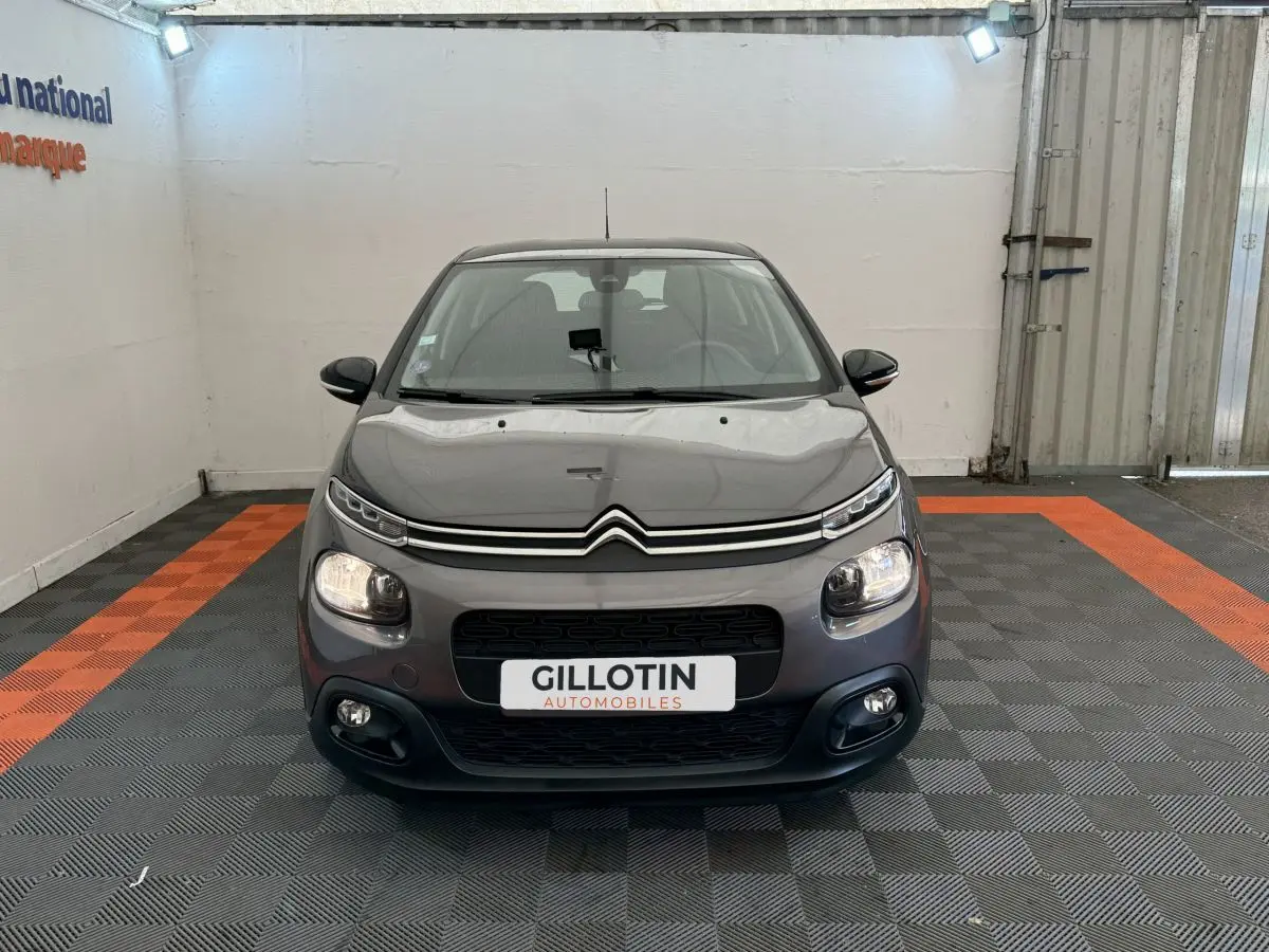 Citroën C3 gris foncé vue de face dans un garage avec phares et antibrouillards allumés.