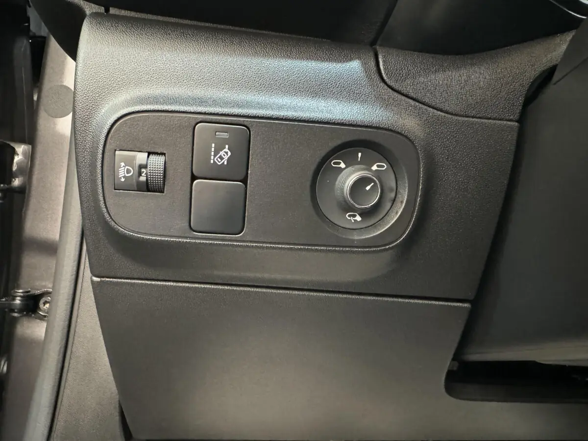 Vue rapprochée des commandes de réglage des rétroviseurs et des phares sur le côté gauche intérieur d'une Citroën C3 gris foncé.