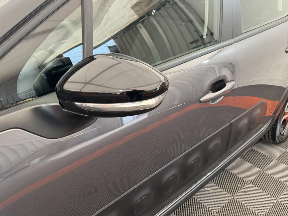 Gros plan sur le rétroviseur noir et la porte côté gauche d'une Citroën C3 gris foncé avec protection latérale noire.
