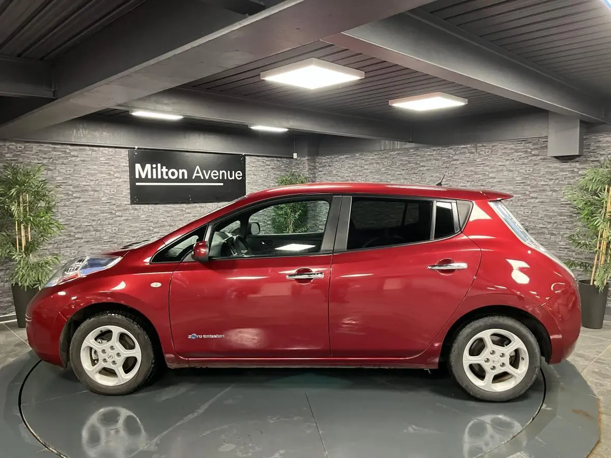 Profil côté gauche d'une Nissan Leaf 30 Visia rouge métallisée, soulignant ses jantes blanches et la mention zéro émission.