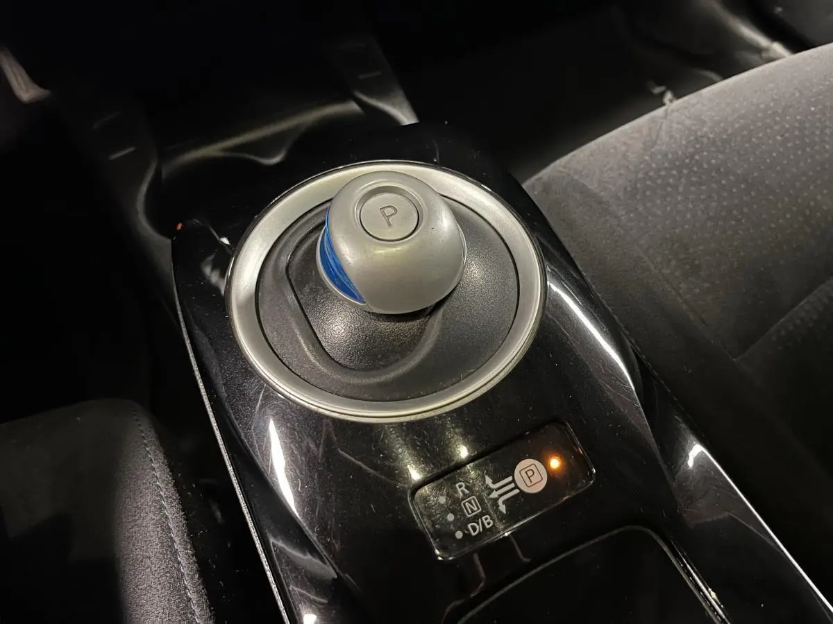 Gros plan sur le levier de vitesses automatique rond et noir avec bouton "P" dans l'habitacle sombre d'une Nissan Leaf rouge 2017.
