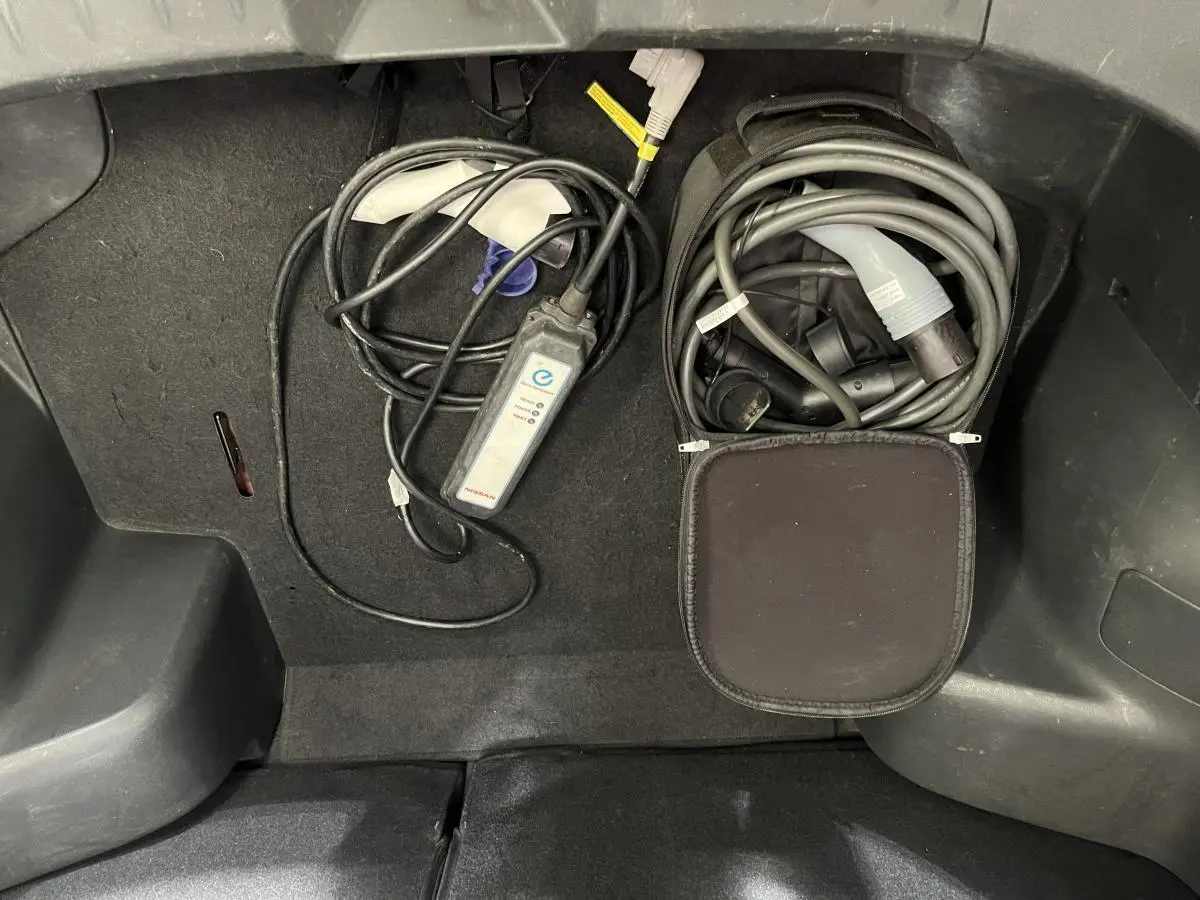 Gros plan sur le coffre d'une Nissan Leaf rouge 2017, montrant les câbles de recharge électrique rangés.