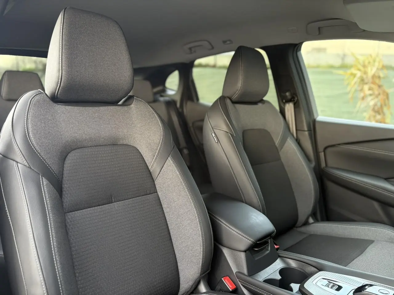 Vue intérieure rapprochée des sièges avant gris et noirs du Nissan Qashqai III e-Power 2025, avec accoudoir central visible.