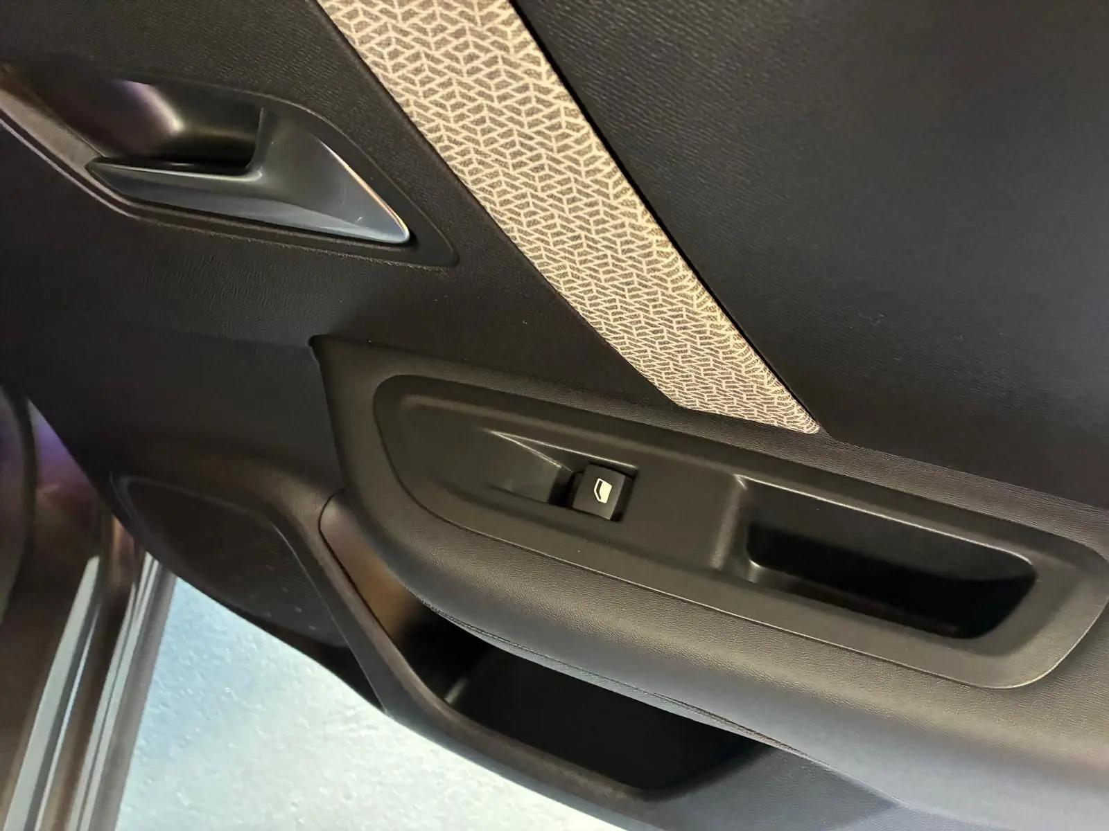 Détail de la porte intérieure côté gauche de la Citroën C4 X 2024, avec bouton de commande de vitre et insert tissu gris à motifs.