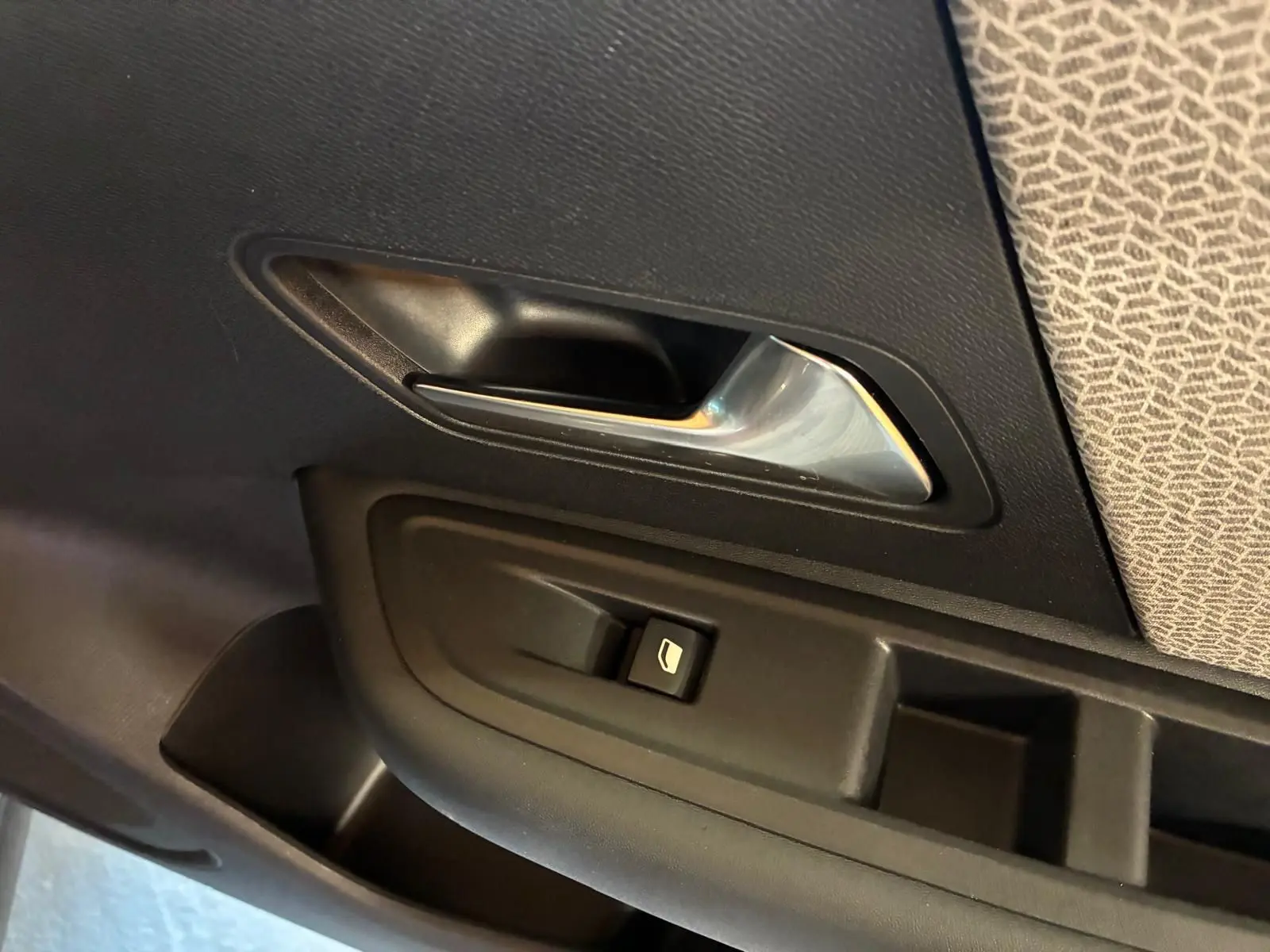 Poignée intérieure et commande de lève-vitre côté gauche d’une Citroën C4 X gris, avec habillage tissu gris clair.
