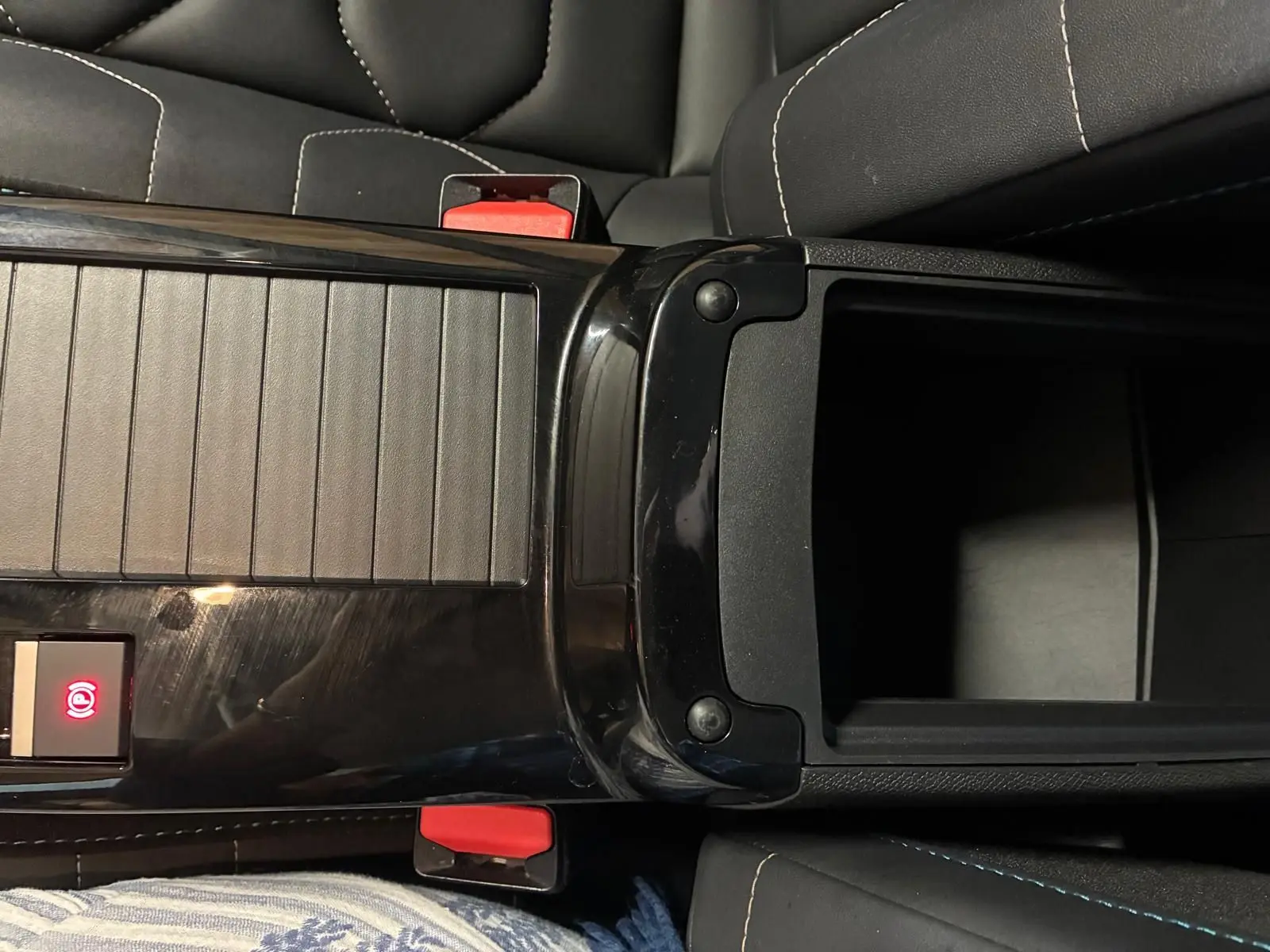 Vue plongeante sur la console centrale noire brillante de la Citroën C4 X 2024 avec accoudoir ouvert et sièges gris foncé.