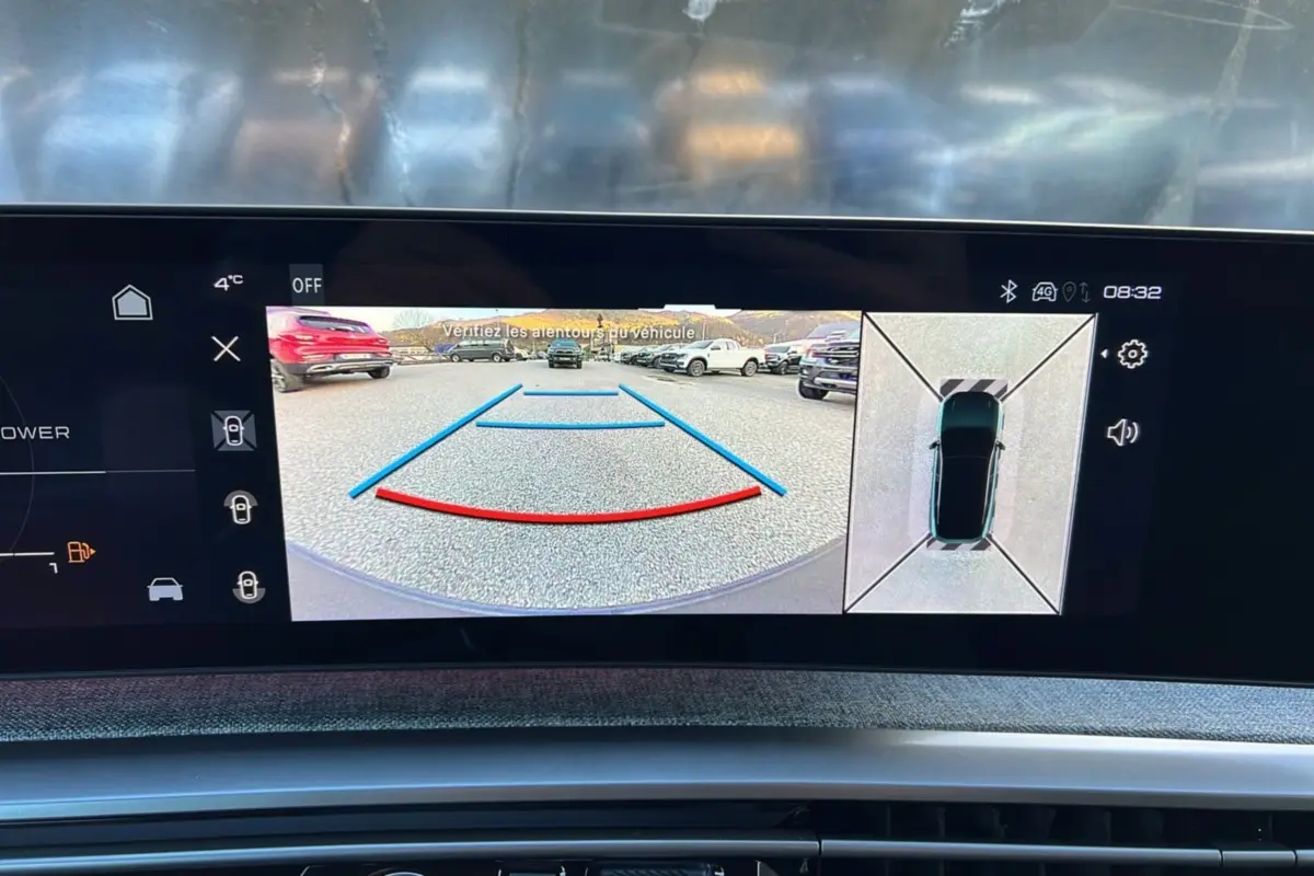 Écran de caméra 360° et recul affichant un parking avec plusieurs véhicules, vue depuis l'habitacle du Peugeot 3008 hybride.