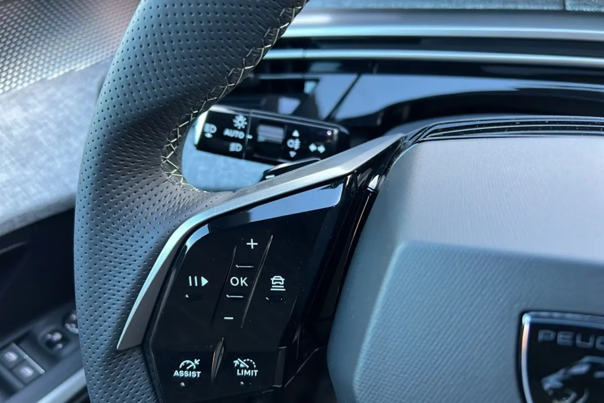 Gros plan sur le volant cuir perforé du Peugeot 3008 Hybrid 145 GT, avec commandes multifonctions et tableau de bord noir brillant.