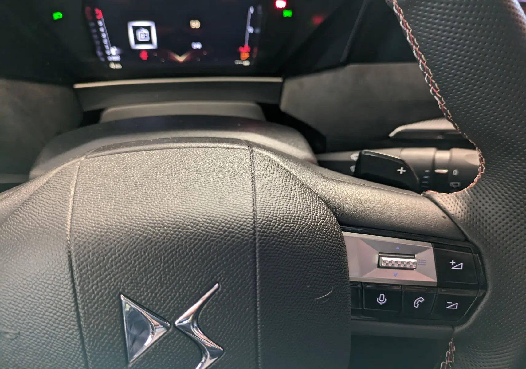 Gros plan sur le volant en cuir noir perforé du DS4 2024, avec logo DS chromé et commandes intégrées visibles.
