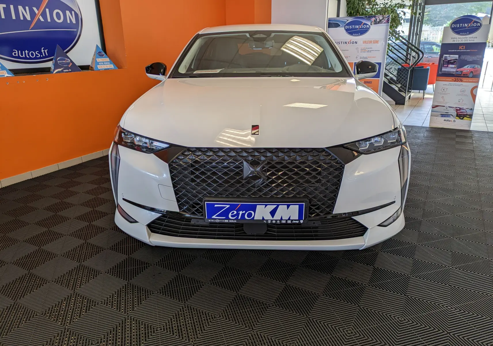 Vue frontale d'une DS4 blanche nacrée avec calandre noire texturée et phares Full LED dans un showroom.