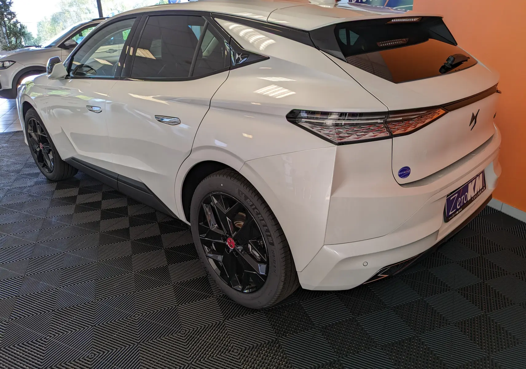 Vue 3/4 arrière droite d'une DS4 blanche nacrée avec jantes alliage noires et feux arrière au design géométrique.