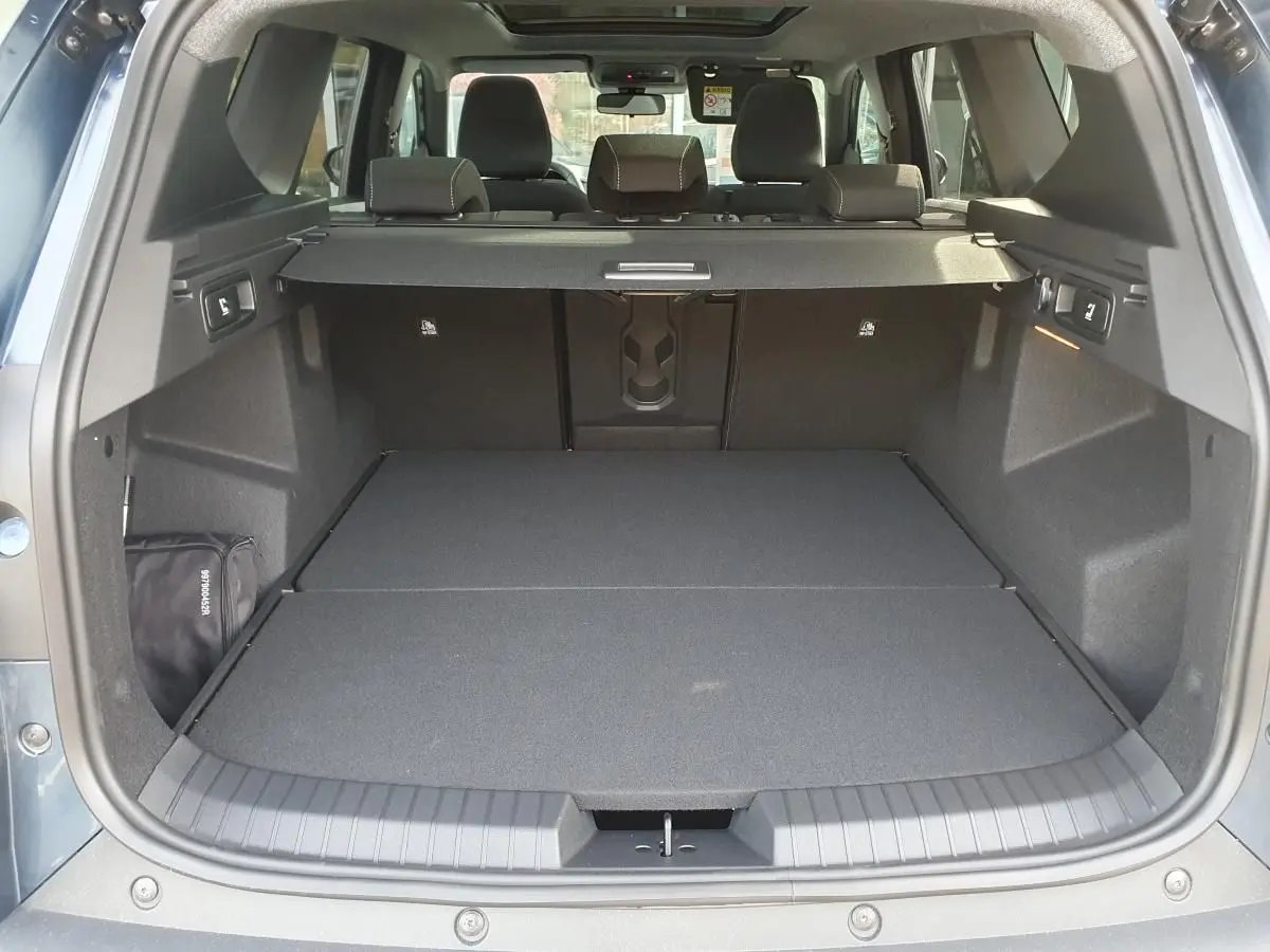 Coffre ouvert vu de l'arrière du Dacia Bigster bleu indigo avec banquette arrière et toit panoramique visibles.