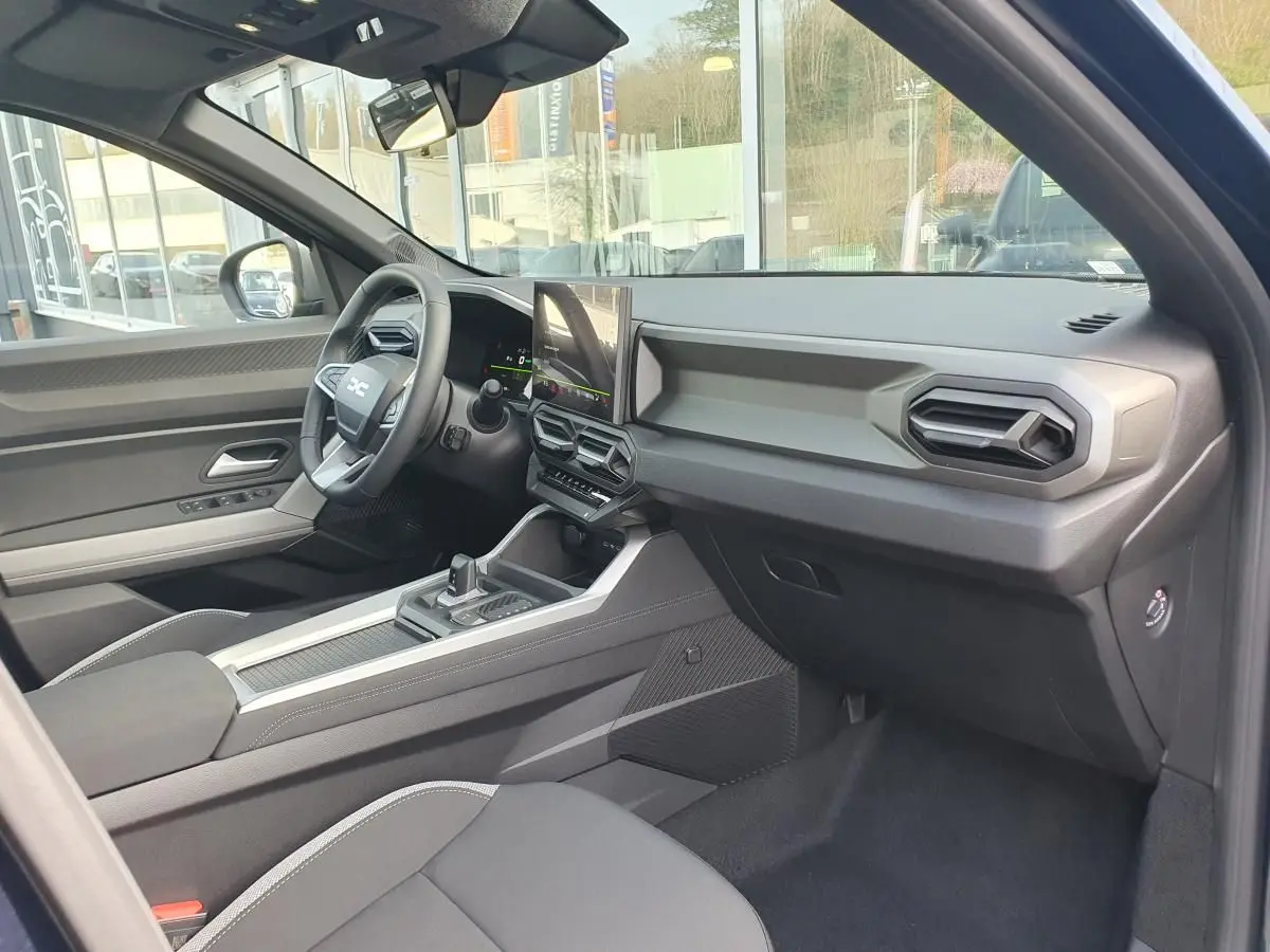 Vue intérieure côté passager du Dacia Bigster bleu indigo, mettant en valeur le tableau de bord moderne et l'écran tactile central.