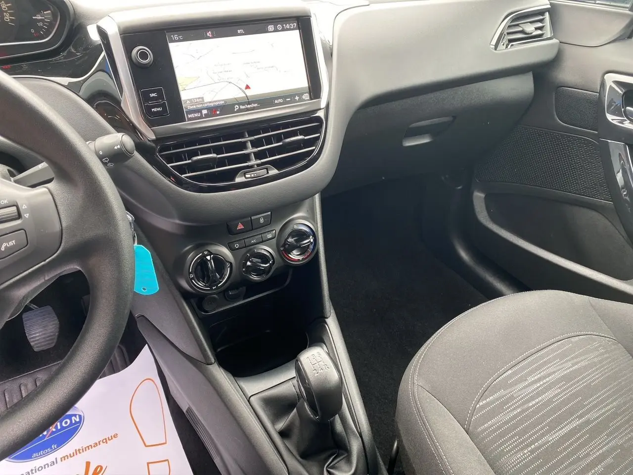 Vue intérieure côté conducteur de la Peugeot 208 Affaire noire, montrant la console centrale avec GPS et boîte manuelle.