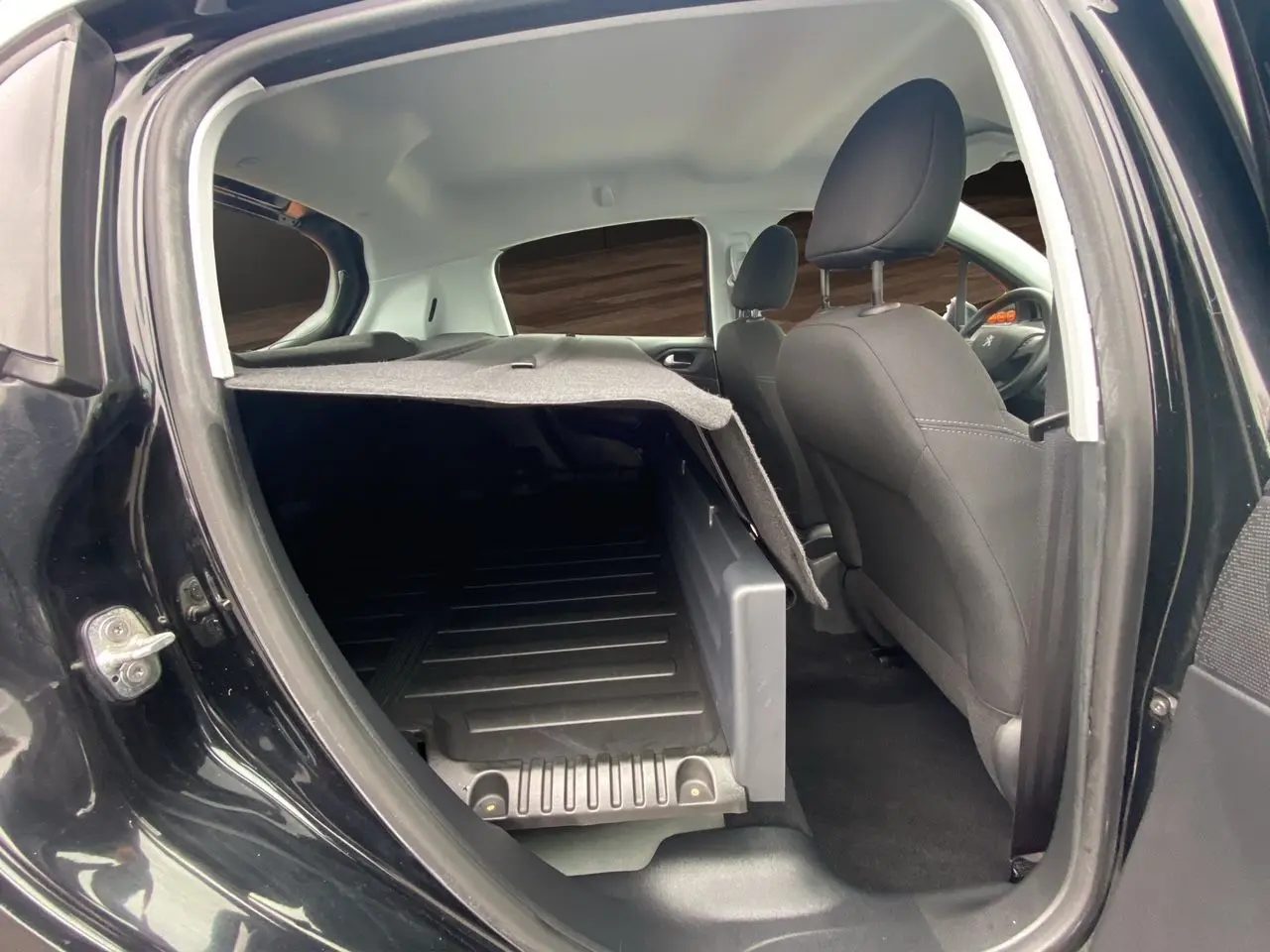 Vue intérieure côté droit arrière de la Peugeot 208 Affaire noire, montrant les sièges avant et l'espace de chargement avec tablette relevée.