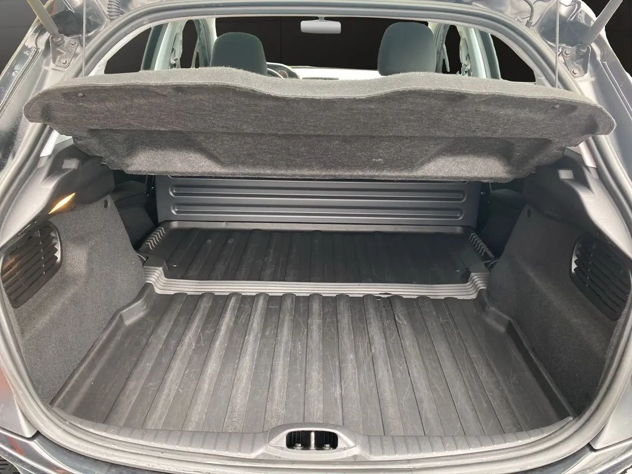 Coffre ouvert d'une Peugeot 208 Affaire noir, vue arrière montrant l'espace de chargement avec tapis en caoutchouc.