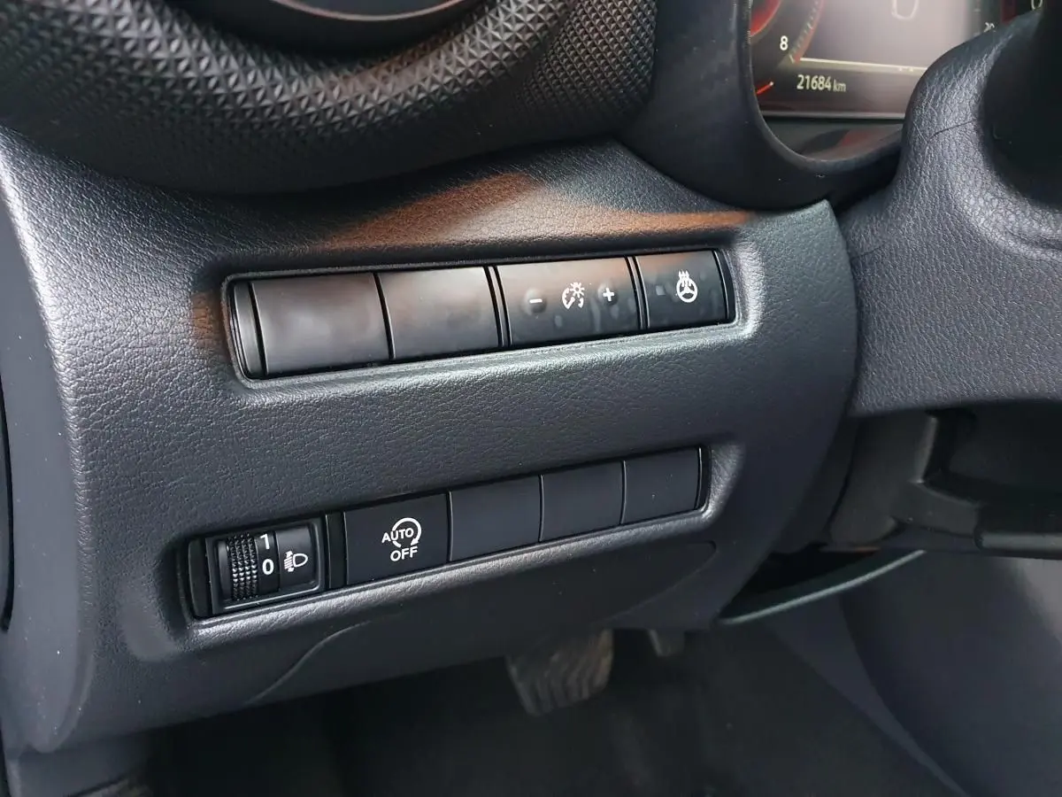 Gros plan sur les commandes de réglage d'éclairage et de chauffage du volant côté gauche du tableau de bord noir du Nissan Juke gris céramique 2025.