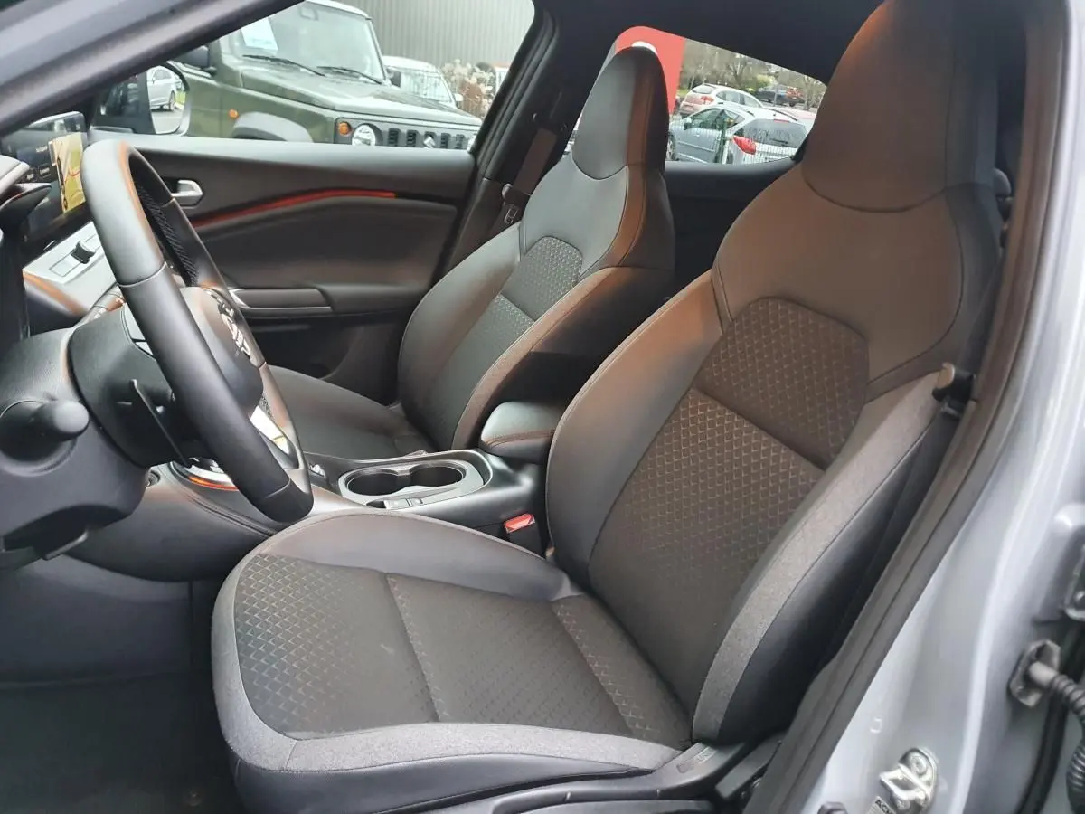 Intérieur du Nissan Juke 2025 en gris céramique, vue côté conducteur sur les sièges avant et console centrale avec porte-gobelets.