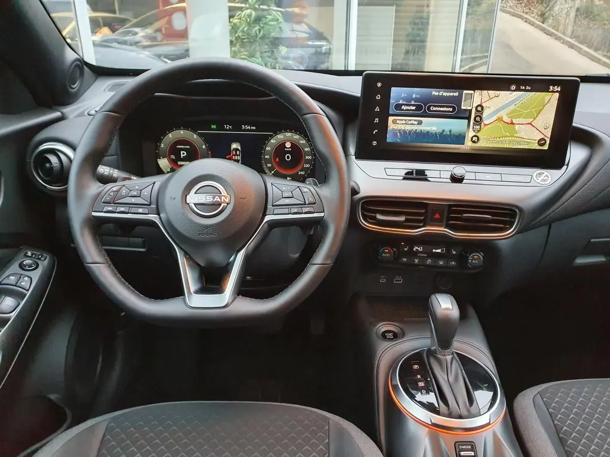 Vue intérieure avant du Nissan Juke 2025 avec volant multifonction, écran tactile 12,3 pouces et levier de boîte automatique.