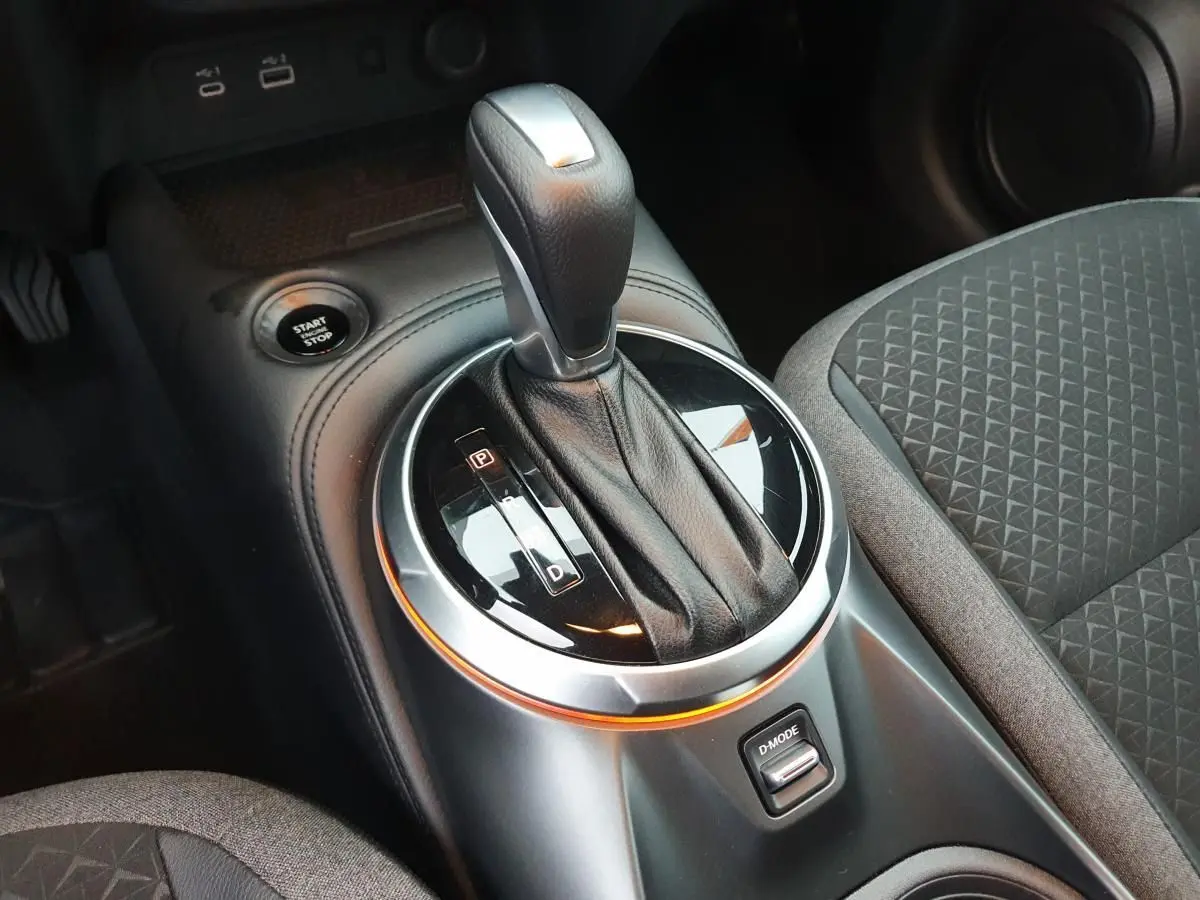 Gros plan sur la console centrale du Nissan Juke 2025 avec levier de vitesse automatique et bouton D-MODE, sièges gris à motifs.