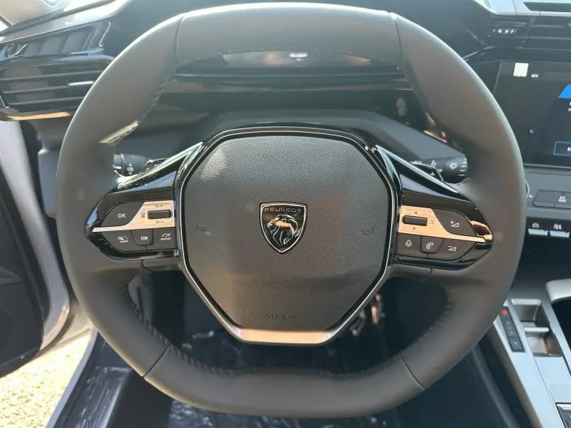Vue rapprochée du volant multifonction noir de la Peugeot 308 2025 avec logo lion au centre et commandes intégrées.