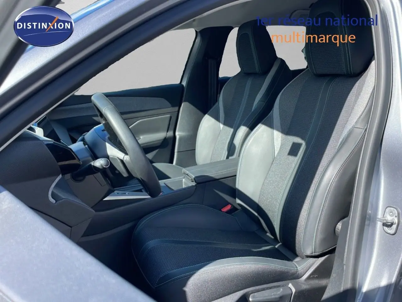 Vue intérieure côté gauche de la Peugeot 308 SW Hybrid 2025, sièges en tissu et cuir gris, volant multifonction.