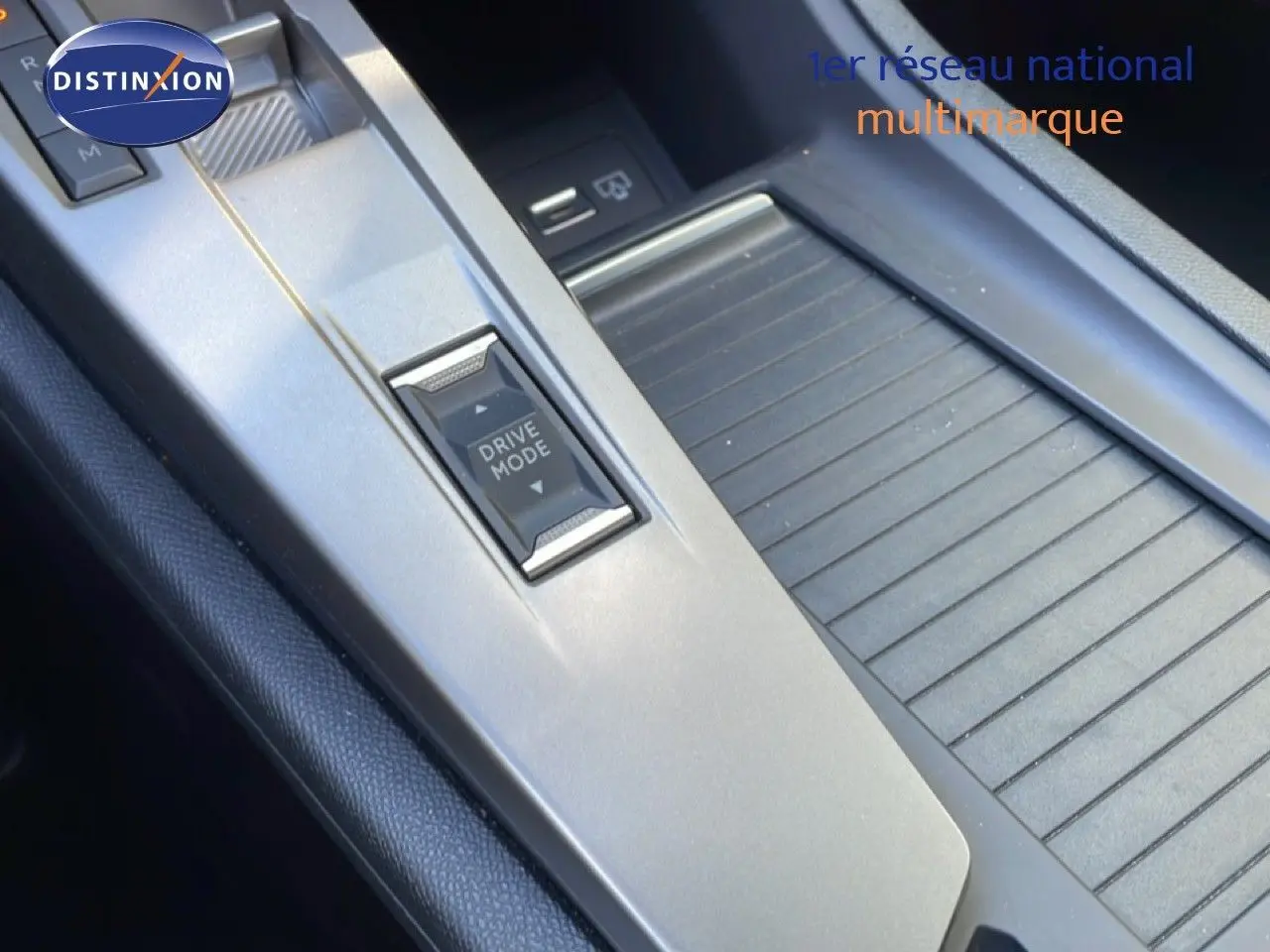 Gros plan sur la console centrale grise du Peugeot 308 SW Hybrid 2025, mettant en valeur le bouton Drive Mode et le rangement adjacent.